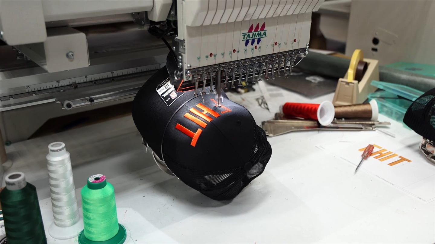 An embroidery machine stitching a logo on a black cap