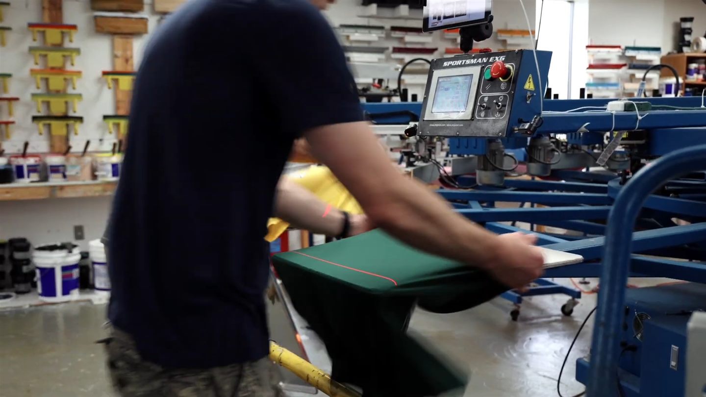 A printer loading a shirt onto the screen printing press