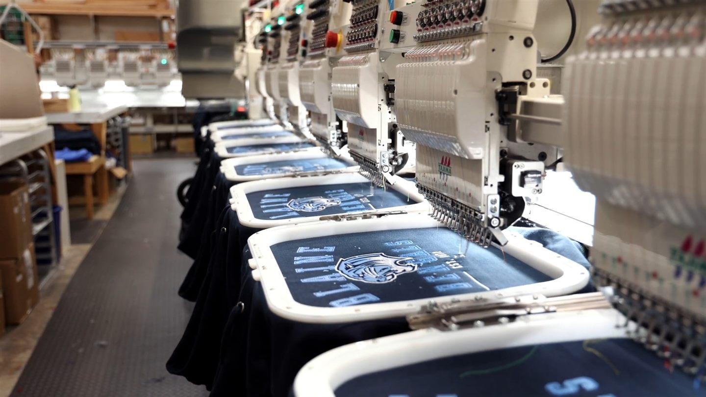 Embroidery machines stitching a team logo on a row of jackets in the Lettermen Sports shop
